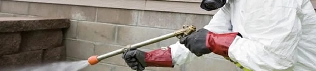 Pest control technician applying exterior insect treatment along a home foundation in Raleigh, NC