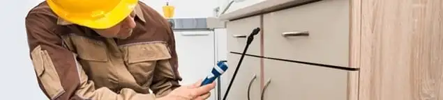 Roach exterminator applying treatment under kitchen cabinets in Raleigh, NC