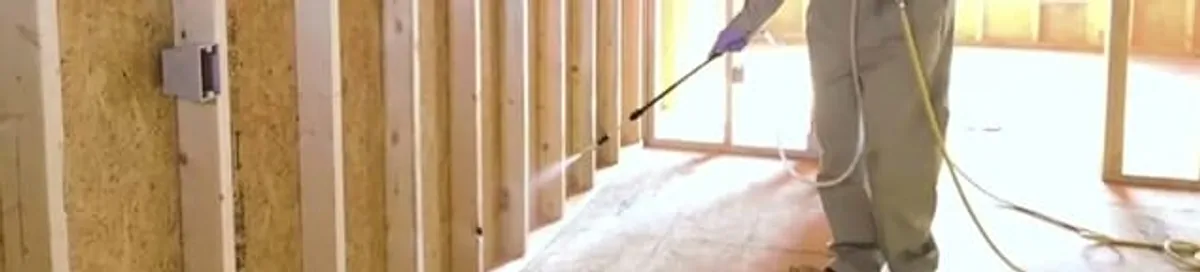 Termite treatment technician applying spray along framing and unfinished walls in Raleigh, NC