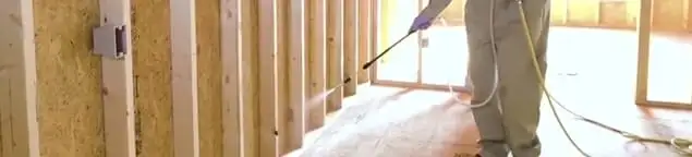 Termite treatment technician applying spray along framing and unfinished walls in Raleigh, NC